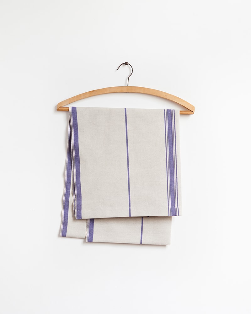 The Mungo Linen Lisburn Table Runner in All Blue, displayed here on a wooden hanger.