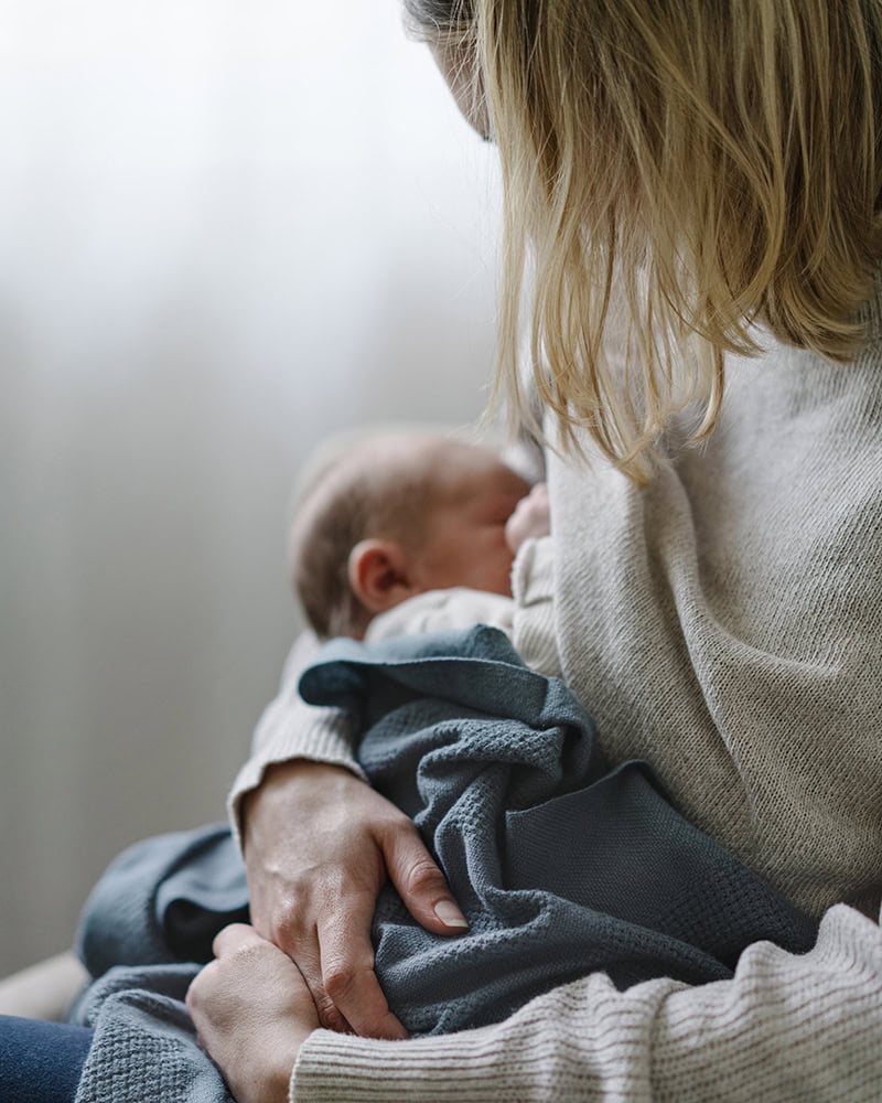 Mom holding baby wrapped in Mungo Cot Baby Blanket woven from 100% Organic Cotton in Spruce.