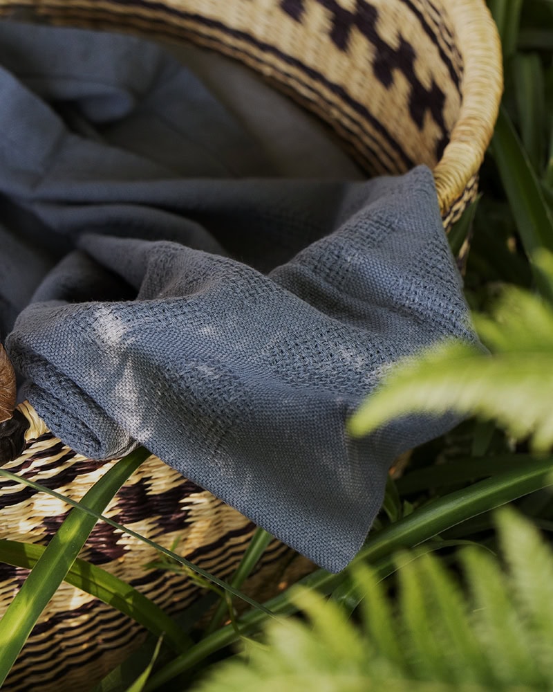 Mungo Cot Baby Blanket in basket place on grass in Spruce.