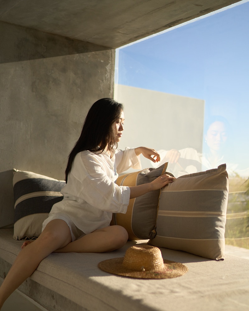 Model seated by a window interacting with Lisburn cushions