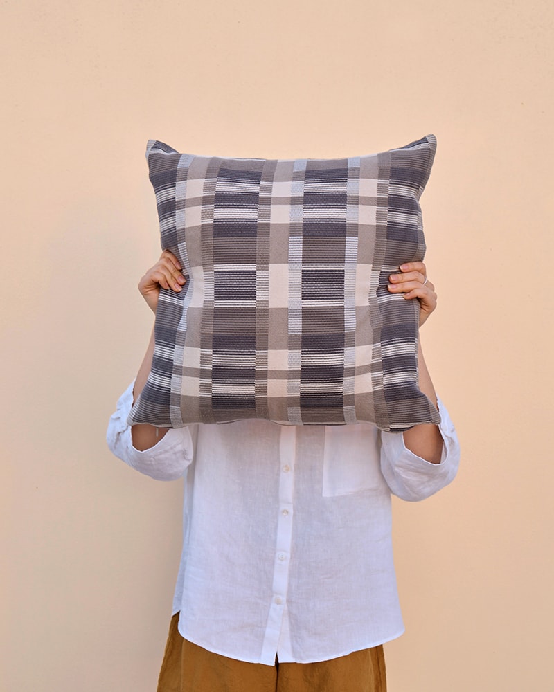 A model covering her face with a colourful checked Skipping Block Cushion Cover. Scatter cushions woven by Mungo in 100% cotton.