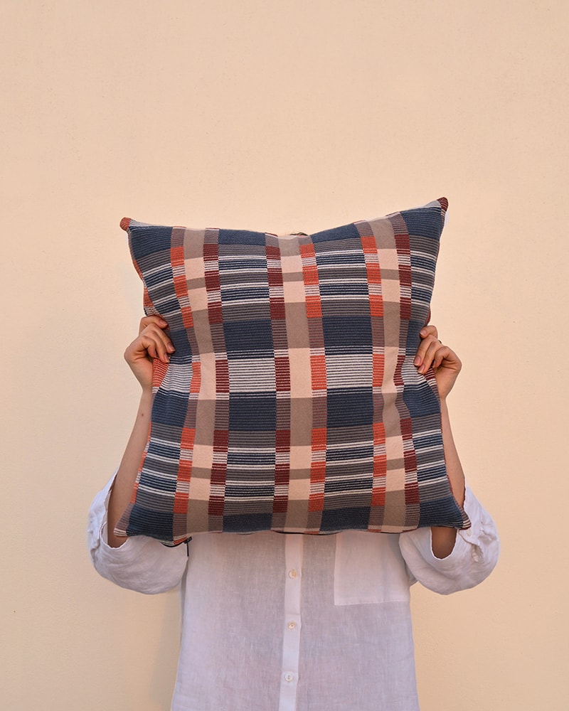 A model blocking her face with a colourful checked cotton Skipping Block Cushion Cover. Woven by Mungo in South Africa.