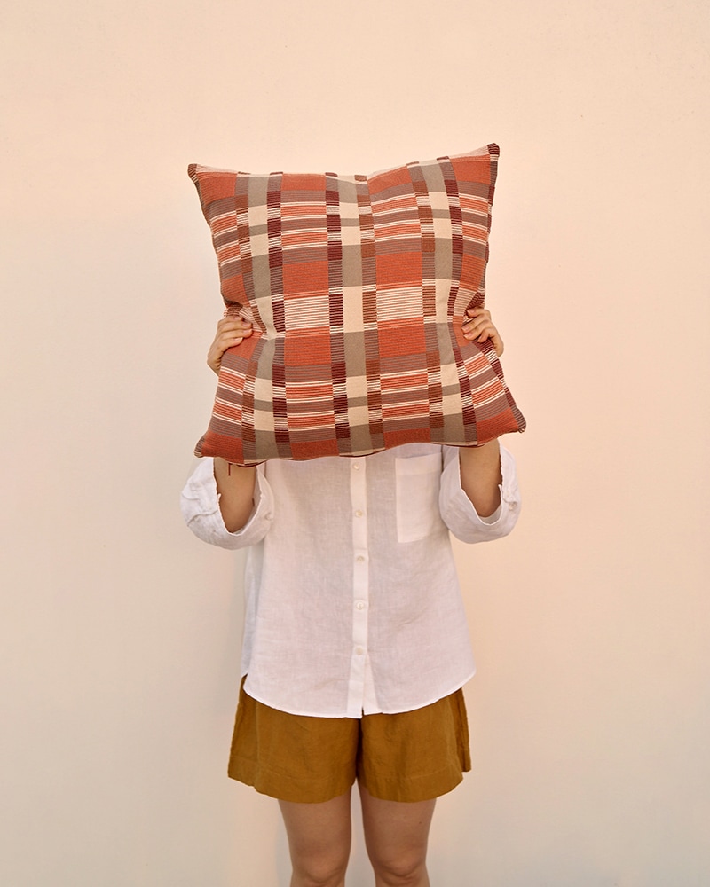 A model blocking her face with a Mungo Skipping Block Cushion Cover. Checked cotton scatter cushions.