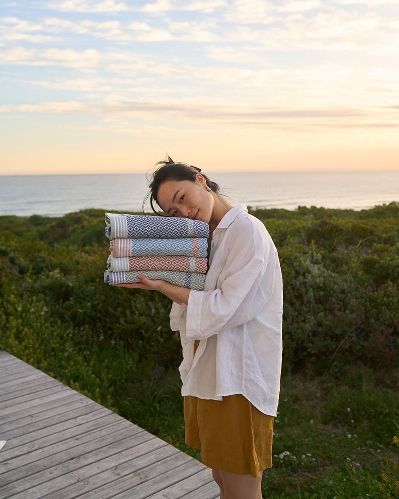 A model with with a stack of Mungo towels. Made with 100% cotton for bath or beach.