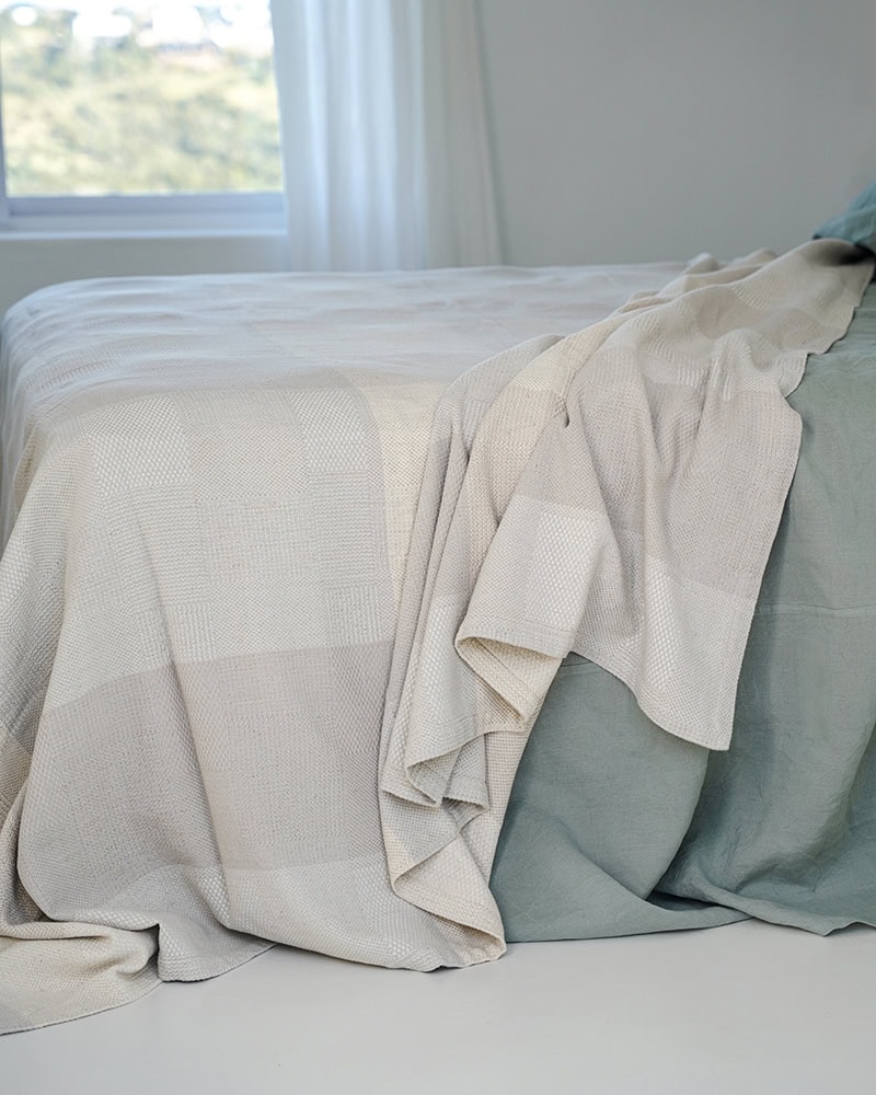 Side view of the The linen and cotton Monsoon Savannah Blanket laying on a bed