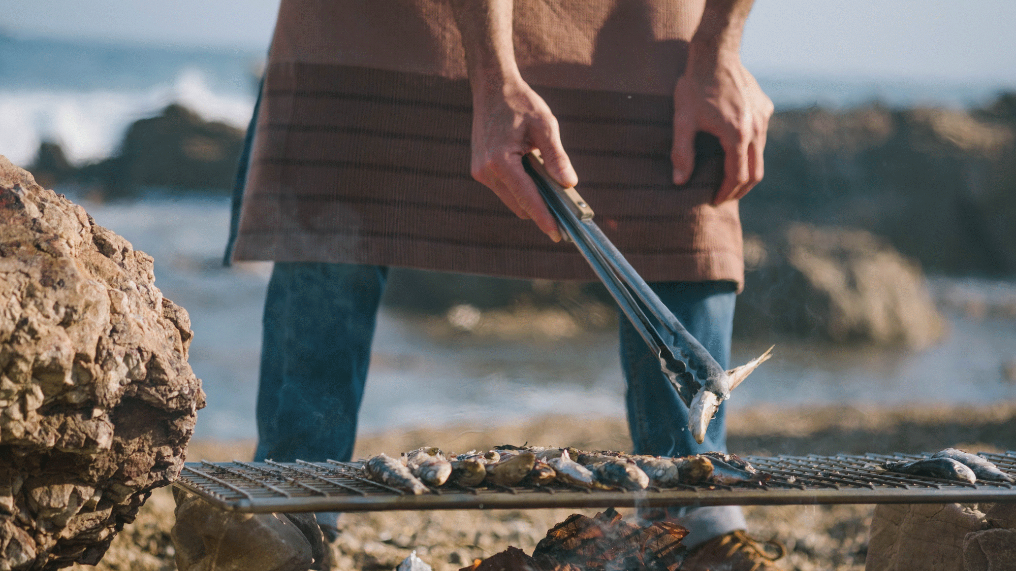 Banner image of a man grilling fish wearing the Grill Apron