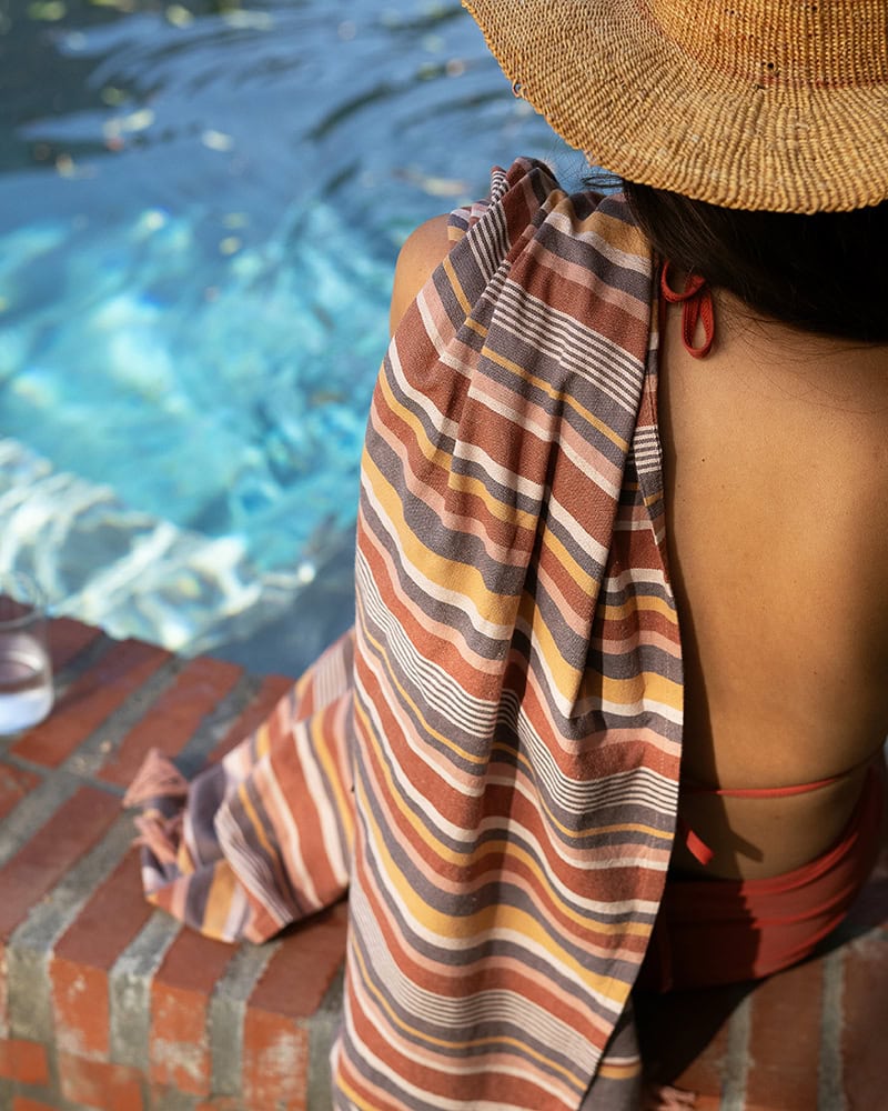 Model sitting by pool with the South Kikoi, a 100% cotton wraps, in Shell over her shoulder
