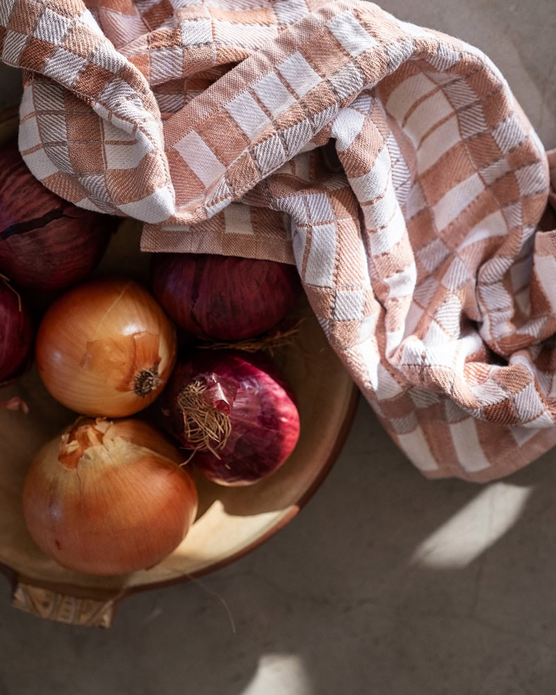 The Pocket Weave Tea Towel in Papaya next two a vegetable bowl, displaying its pink blocks and double sided weave