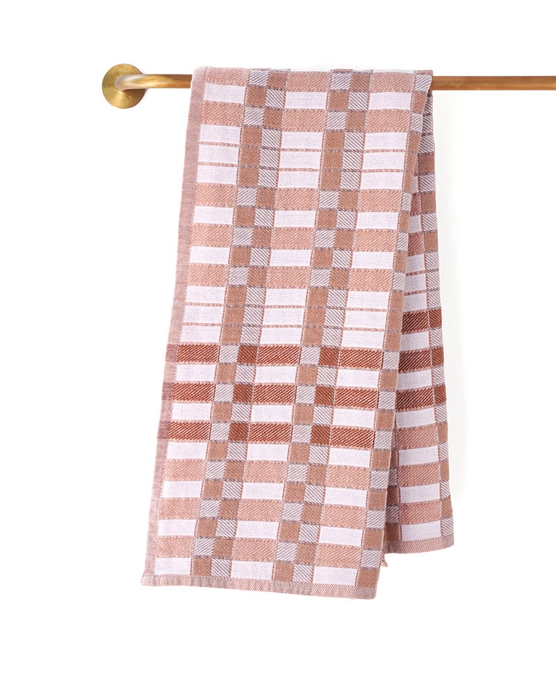 The Mungo Pocket Weave Tea Towel in Papaya hanging over a rail, displaying it's unique block design and woven with 100% Organic cotton.